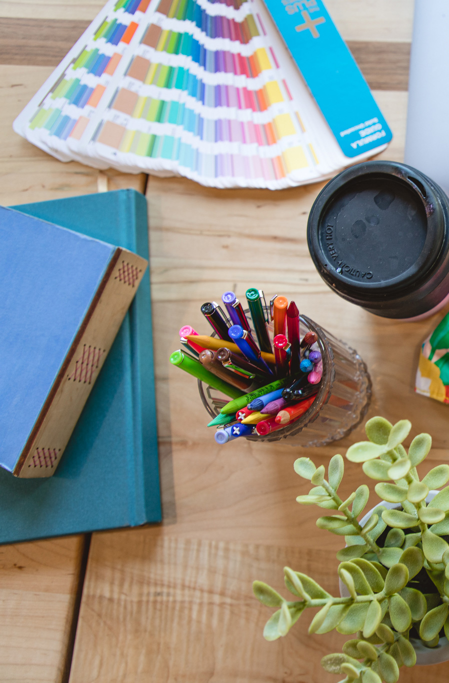 Colorful desk with journals, pantone books, coffee mug, colorful pens and pencils
