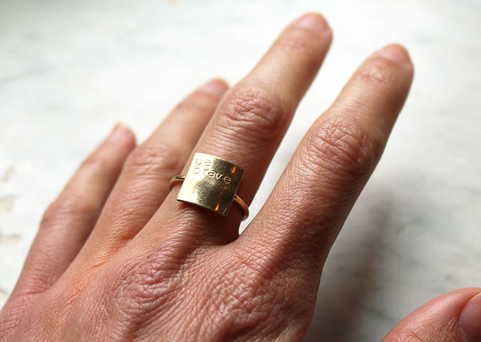 Hand wearing a ring with text Be Brave stamped into it