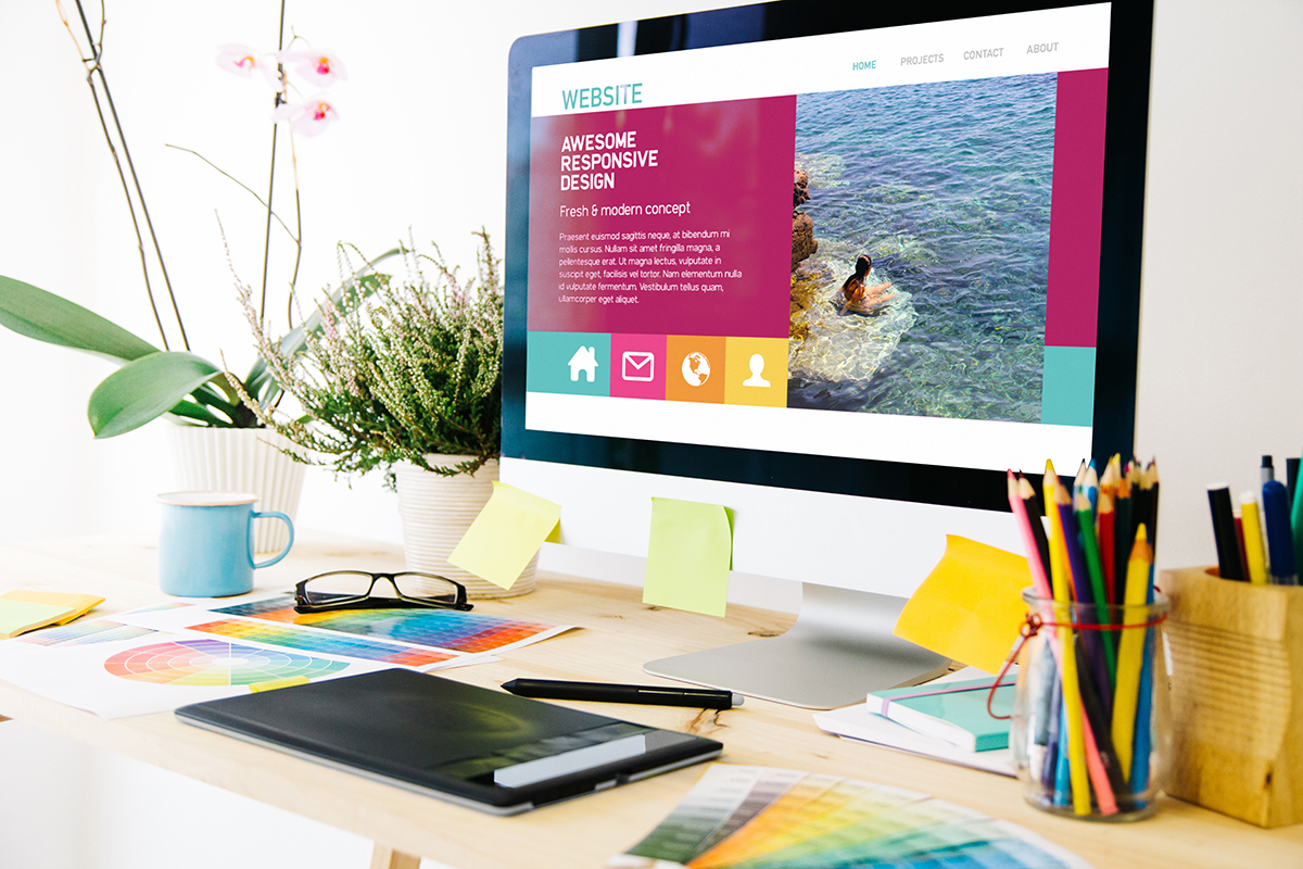 Colorful office desk with desktop computer, tablet and colored pencils, responsive web design in the monitor